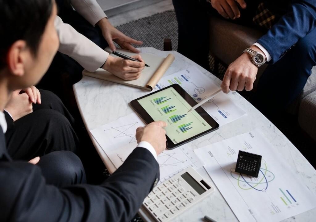 Team discussing analytics on tablet with transaction coordinator software to save time and manage real estate transactions efficiently